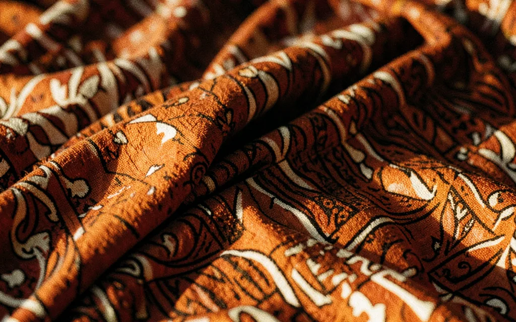 Close-up of folded wax print cotton in ochre and terracotta, raking light across the weave.